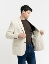 Saco beige de lino con corte clásico, solapas de muesca, cierre de dos botones, bolsillos laterales con solapa y bolsillo en el pecho.