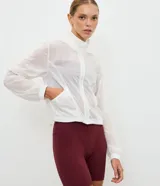 Campera cortavientos deportiva modelo cropped, color blanco traslúcido, con cierre frontal de cremallera, capucha estructurada, puños elásticos y bajo ajustable con cordón.