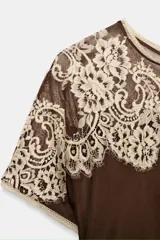 Vestido midi de viscosa color marrón oscuro, con cuello redondo y manga corta. Presenta un canesú de encaje floral color beige claro que cubre los hombros y parte superior del pecho. El bajo es evasé.