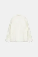 Camisa de corte holgado confeccionada en tejido satinado con mezcla de lyocell. Presenta cuello redondo con escote en pico y lazada frontal integrada. Cuenta con mangas largas abullonadas terminadas en puños anchos y bajo recto.