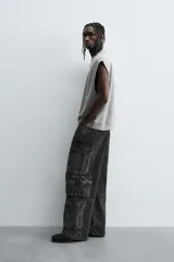 Pantalón cargo de denim lavado negro, corte relajado y tiro medio. Presenta múltiples bolsillos cargo con solapa y detalle de cierre en las perneras, además de bolsillos de vivo traseros. El bajo es ajustable con trabilla.