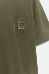 Camiseta de algodón con efecto lavado, cuello redondo y manga corta. Presenta un detalle de fornitura metálica aplicada en el pecho.