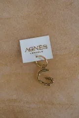 Caravana individual en forma de argolla dorada con dije colgante en forma de letra con textura rústica.
