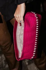 Sobre tipo baguette confeccionado en cuero con textura croco en color fucsia. Presenta un diseño con detalles artesanales de trenzado en contraste y una base en tono bordó. Incluye un lazo desmontable para usar como cartera.