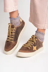 Zapatillas bajas de cuero color marrón con estrella beige en el lateral, cordones color beige y detalle dorado en el talón.