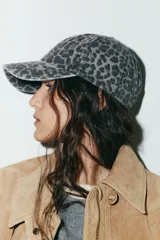Gorra con visera confeccionada en sarga de algodón 100%, con estampado animal print en tonos grises y negros. Presenta costuras marcadas y ajuste en la parte posterior.
