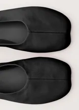Zapato plano tipo chatita, de color negro, confeccionado en piel de ovino con diseño minimalista y puntera cuadrada.