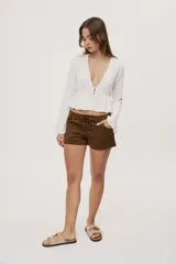 Short de tiro bajo con textura efecto gamuza color beige, bolsillos delanteros y detalle de cordones entrecruzados en la parte frontal.