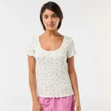 Camiseta de manga corta de punto canalé en color blanco, con estampado de pequeñas flores y terminaciones con volados en cuello, mangas y ruedo.