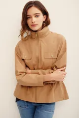 Campera estilo militar color tostado, confeccionada en 100% algodón, con cuello alto, cierre frontal de cremallera, bolsillos con solapa en el pecho y cordón ajustable en la cintura.