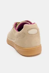 Zapatilla deportiva de gamuza en color beige, con cordones y forro interior en color fucsia, montada sobre una suela de goma color caramelo.