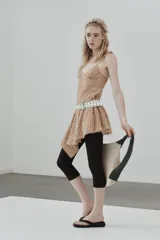 Vestido corto con escote en V y tirantes finos ajustables, confeccionado en tejido a cuadros beige y rojo. La falda es asimétrica y presenta un bajo con detalle de encaje.