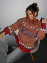 Sweater tejido con técnica intarsia, de silueta holgada y cuello a la base. Presenta un diseño con motivos geométricos, detalles de flecos colgantes y terminaciones en tejido acanalado en color rojo en puños y ruedo.