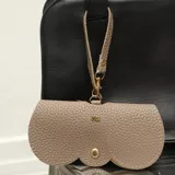 Estuche para lentes de ecocuero negro con textura granulada, diseño minimalista con cierre de broches metálicos dorados y correa de mano desmontable.