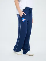 Pantalón de jogging azul marino con cordón ajustable en la cintura, bolsillos laterales y líneas blancas laterales. Presenta el escudo del Club Nacional de Football y el logo de Umbro bordados.