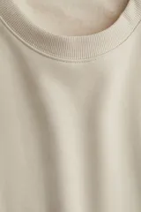 Buzo de tejido liso color crema, con cuello redondo acanalado, hombros caídos y puños y bajo acanalados.