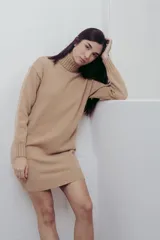 Vestido corto de tejido de punto en color beige, con cuello alto y mangas largas. Presenta puños y ruedo acanalados, con un diseño de calce relajado.
