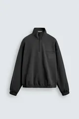 Sudadera de corte relajado color negro, con cuello alto y cierre frontal de cremallera. Presenta un bolsillo de vivo en el pecho con un estampado a contraste y acabados elásticos en puños y ruedo.