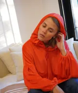 Buzo oversize de plush color naranja, con capucha ajustable por cordones, bolsillo canguro delantero y mangas largas abullonadas con puños elásticos.