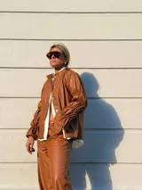 Camisa de cuero sintético color marrón, con cuello redondo, cierre frontal de botones y mangas largas con diseño fruncido y volados en los puños.