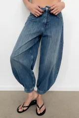 Jeans de tiro medio y diseño balloon, color azul denim con efecto lavado, cinco bolsillos, cierre frontal con cremallera y botón metálico, y bajos acabados en puño.