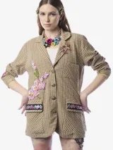 Blazer de corte recto con estampado de cuadros en tonos beige y verde. Presenta cierre frontal con botones metálicos decorativos, solapa clásica, bolsillo superior tipo parche y dos bolsillos inferiores con solapa adornados con bordados florales. Incluye una aplicación floral bordada con lentejuelas en el frente y parches en los codos en contraste.