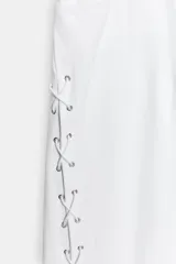 Jeans rectos de tiro medio en color blanco, con cinco bolsillos, trabillas y cierre frontal con cremallera. Presenta detalle de cordones cruzados con ojalillos metálicos a lo largo de los laterales de ambas piernas.