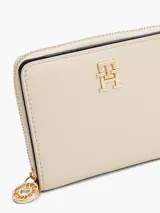 Billetera Tommy Hilfiger color crema con cierre de cremallera y logo TH dorado en el frente.