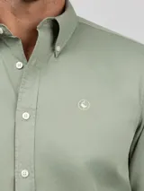 Camisa de hombre color azul, con cuello buttondown, cierre frontal con botones y logo bordado en el pecho. Presenta un acabado vintage logrado mediante el proceso de teñido en prenda.