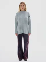 Buzo tejido de punto color beige, con cuello subido, diseño oversized y aberturas laterales en el ruedo.