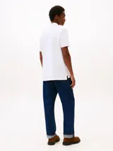 Chomba blanca de corte regular confeccionada en algodón orgánico con un toque de elastano, cuello tipo chomba y cartera de dos botones. Tiene el logo de Tommy Hilfiger bordado en el pecho.