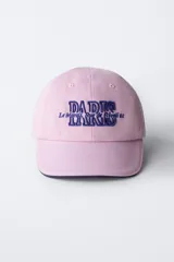 Gorra de béisbol azul marino con visera curva y detalle de borde en color crema. Presenta un bordado frontal con la palabra 'LONDON' en tipografía estilo varsity y texto adicional debajo.