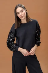 Sweater negro de cuello redondo con mangas largas decoradas con lentejuelas brillantes del mismo tono. Presenta puños y ruedo acanalados, con un corte relajado y cómodo.