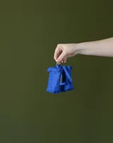 Charm en forma de mini mochila acolchada color azul, con cierre superior y mosquetón metálico para colgar.