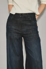 Jean de corte oxford y tiro alto, confeccionado en denim azul oscuro con un ligero lavado. Presenta un diseño de pierna ancha que se ensancha desde la cadera hacia el ruedo, con cierre y botón frontal.