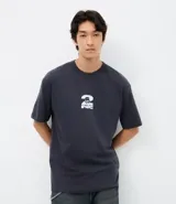 Remera de corte relajado color gris oscuro, con cuello redondo y manga corta. Presenta una estampa frontal pequeña en color blanco con el logo de Tupac.