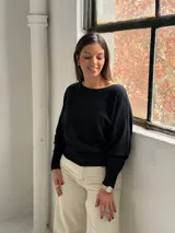 Sweater negro de punto con diseño de mangas tipo murciélago, cuello redondo y puños ajustados. Presenta un sutil patrón de líneas verticales en el tejido.