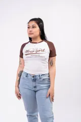 Remera tipo baby tee de diseño raglán, color blanco con mangas y ribete del cuello en marrón. Cuenta con estampa frontal con la leyenda 'New York Brooklyn Durability and Strength'.