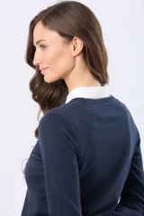 Buzo tejido en hilo de algodón color beige, con cuello redondo y manga larga. Presenta un corte clásico y un pequeño detalle metálico en la parte inferior izquierda.