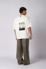 Remera de corte oversize en color crudo, con cuello redondo y mangas cortas. Presenta un pequeño estampado gráfico minimalista en el lado derecho del pecho.