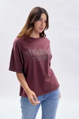 Remera de manga corta con corte boxy, color bordó con efecto de teñido especial. Presenta una estampa frontal con el texto 'STOKHOLM FASHION ARCHIVE CREATIVE SPACE' en tono oscuro.