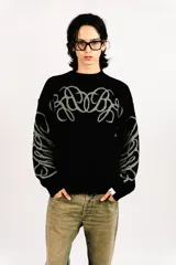 Sweater reversible de tejido de punto con diseño gráfico estilo tribal. Un lado presenta base negra con detalles en gris, mientras que el otro lado presenta base gris con detalles en negro. Posee cuello redondo, mangas largas y puños acanalados.