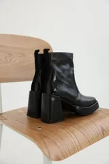 Botas de cuero negro con taco cuadrado alto, plataforma y puntera cuadrada. Presentan cierre lateral y detalles en charol y gamuza en la parte trasera.