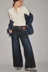 Jean de corte oxford y tiro alto, confeccionado en denim azul oscuro con un ligero lavado. Presenta un diseño de pierna ancha que se ensancha desde la cadera hacia el ruedo, con cierre y botón frontal.