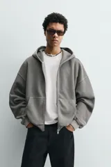 Sudadera tipo hoodie de corte relajado, confeccionada en tejido de algodón con textura estructurada y efecto lavado. Presenta cierre frontal con cremallera, cuello con capucha, manga larga, bolsillos tipo canguro y acabados en rib.