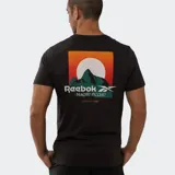 Remera negra de algodón con cuello redondo y manga corta. Presenta un estampado pequeño en el pecho con el logo de Reebok y un diseño de montañas en tonos verdes, junto al texto "Machu Picchu National Park".