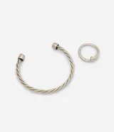 Kit de bijouterie compuesto por una pulsera rígida con diseño trenzado y un anillo minimalista de metal plateado.
