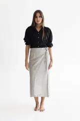 Pollera midi de lino color gris perla con tratamiento acerado. Diseño cruzado tipo portafolio con cierre interno de botón y lazos en la cintura. Cuenta con bolsillos aplicados y bajo asimétrico de corte oriental.