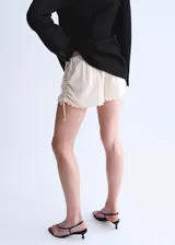 Short mini de viscosa semitransparente color crudo, con diseño bordado, bajo festoneado y cintura ajustable con elástico en los laterales.