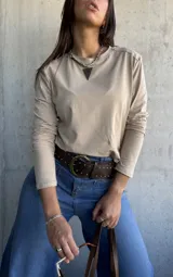 Remera de algodón color beige, de manga larga y cuello redondo, con detalle de tachas metálicas en los hombros.